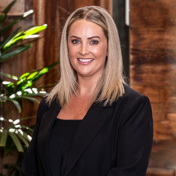 A client manager in a black dress and blazer poses out the back of their Perth Brokers office for a professional headshot